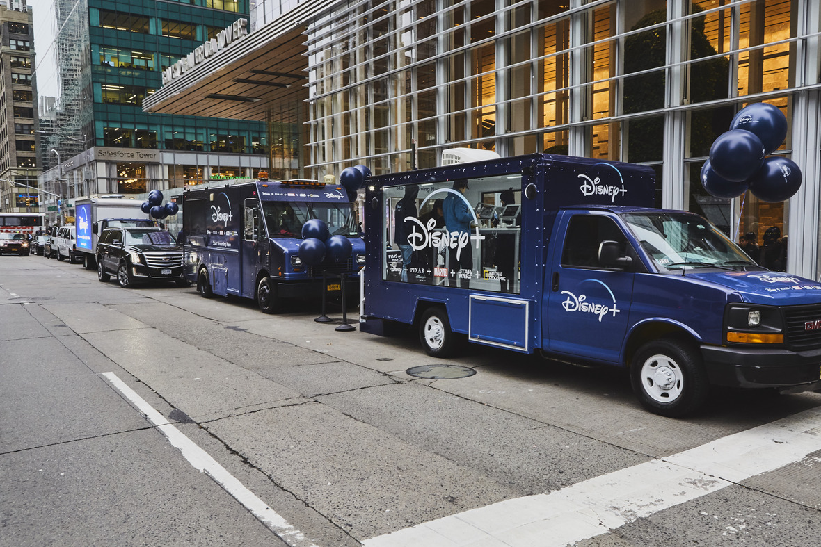 Disney+ branded vehicles lined up on city street for guerrilla marketing campaign, featuring promotional balloons and signage highlighting the streaming service.